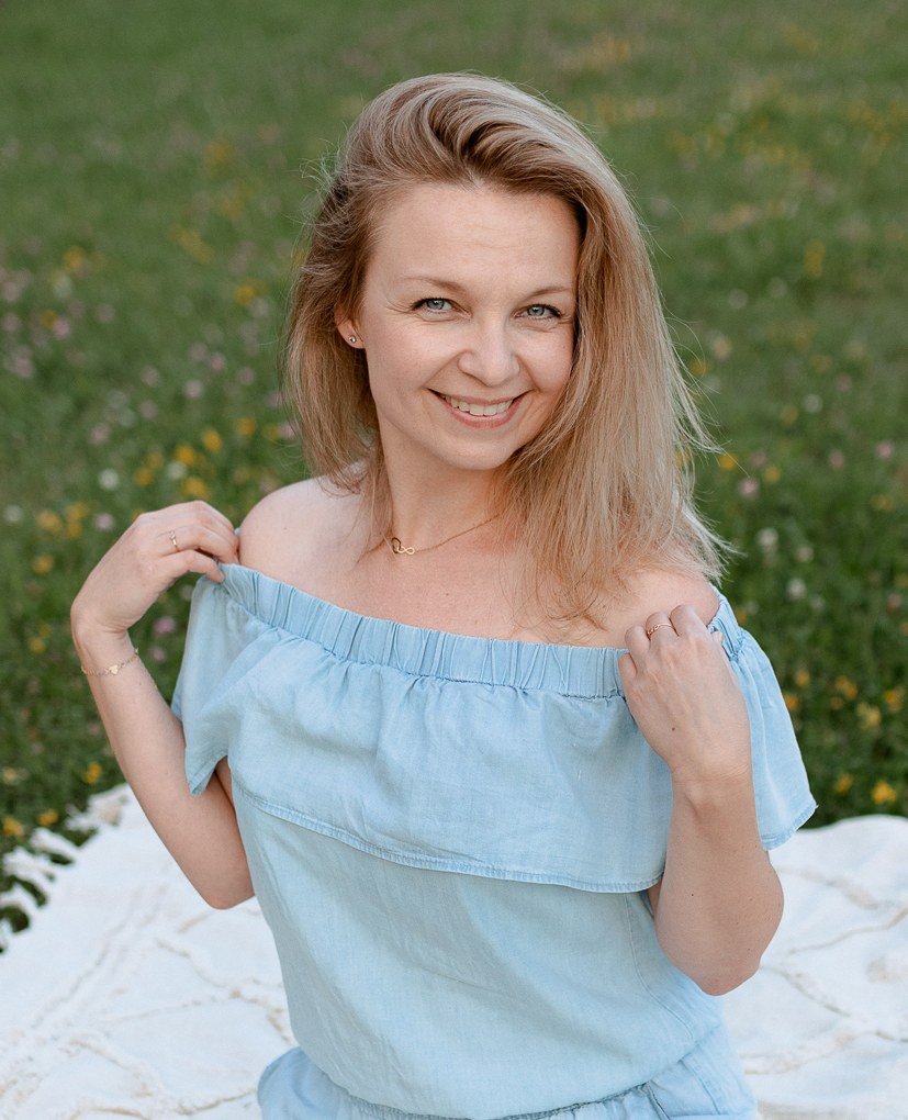 Joanna Rosikoń uśmiecha się, siedząc na kocu na łące.